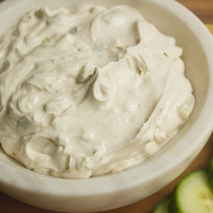 Creamy dairy free tzatziki style sauce in a white bowl served with fresh cucumber slices and lemon wedge