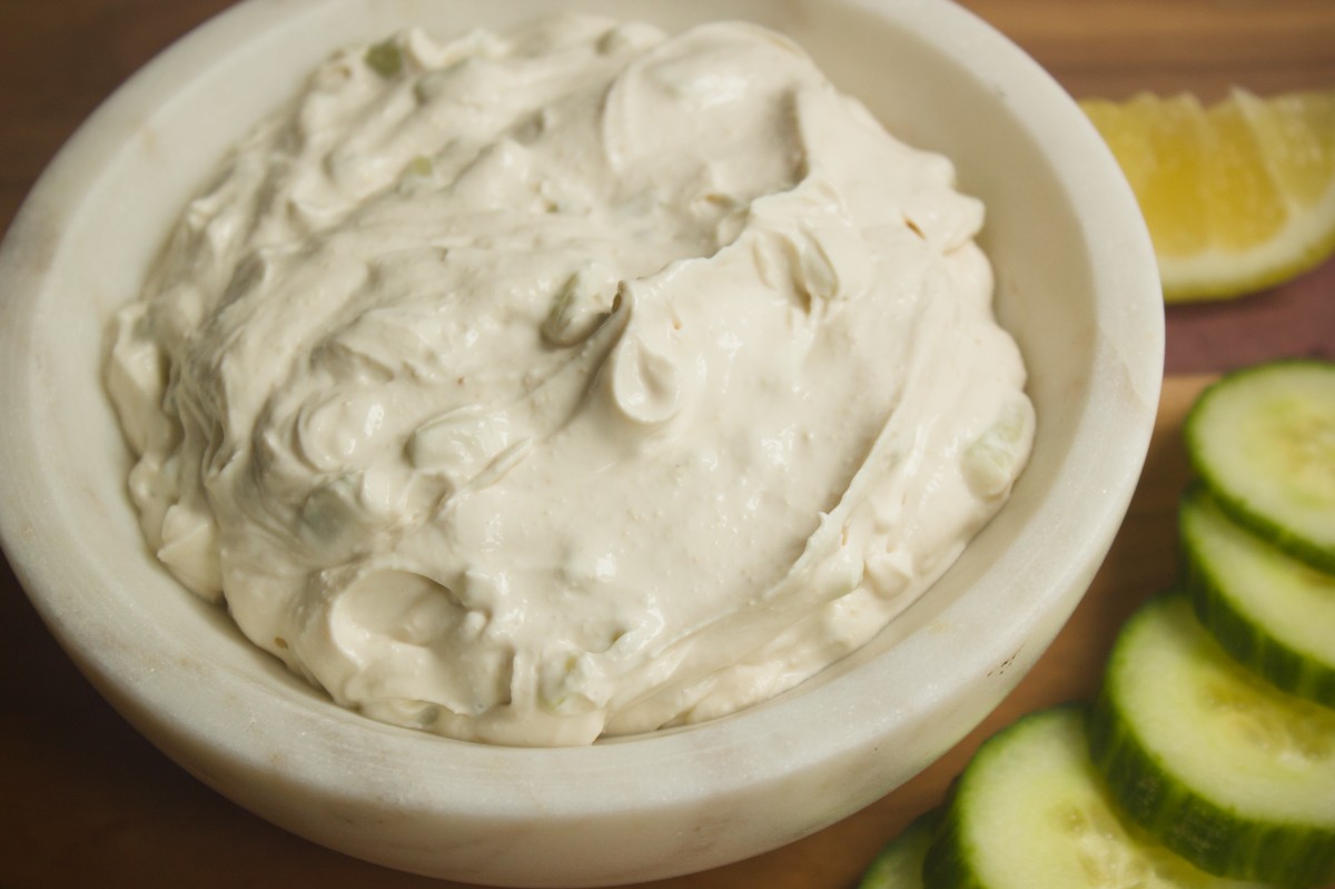 Creamy dairy free tzatziki style sauce in a white bowl served with fresh cucumber slices and lemon wedge