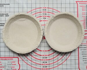 Two round unbaked gluten-free pie shells side by side on a silicone pastry mat