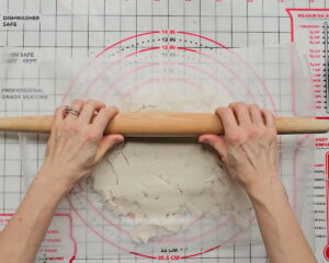 Hands rolling out gluten-free pie crust dough on a silicone pastry mat with a rolling pin