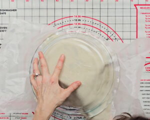 Hands lifting and transferring rolled gluten-free pie crust dough to a glass pie dish