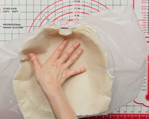 Hands flipping gluten-free pie crust dough into a round glass pie pan