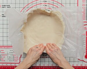 Hands pressing gluten-free pie crust dough evenly into the edges of a pie baking dish