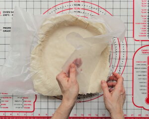 Hand peeling wax paper away from pressed gluten-free pie crust in a pie baking dish