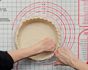 Hands shaping and crimping the edges of a gluten-free pie crust 