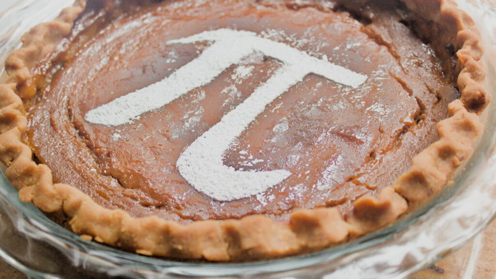 Pumpkin pie in a glass pie dish with powdered sugar pi symbol