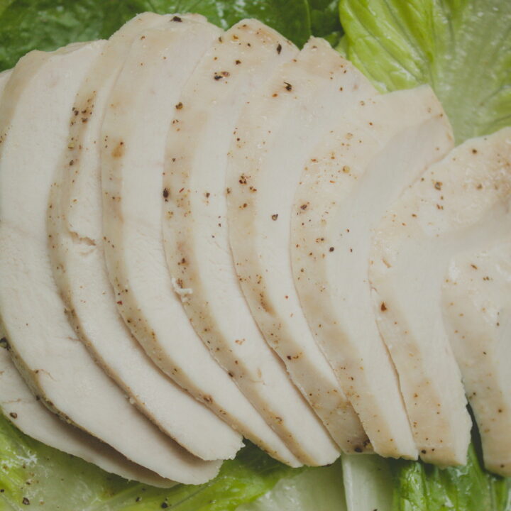 Thinly sliced cooked chicken breast arranged in a fan pattern on a bed of fresh green romaine lettuce leaves, seasoned with black pepper