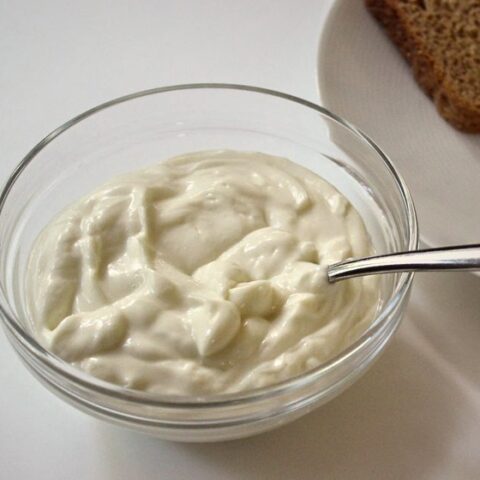 Mayonnaise in a glass bowl next to a plate with slices of bread.