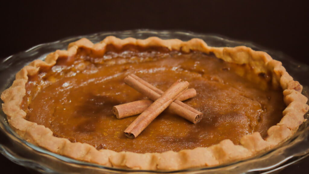 Homemade pumpkin pie in a glass dish topped with cinnamon sticks