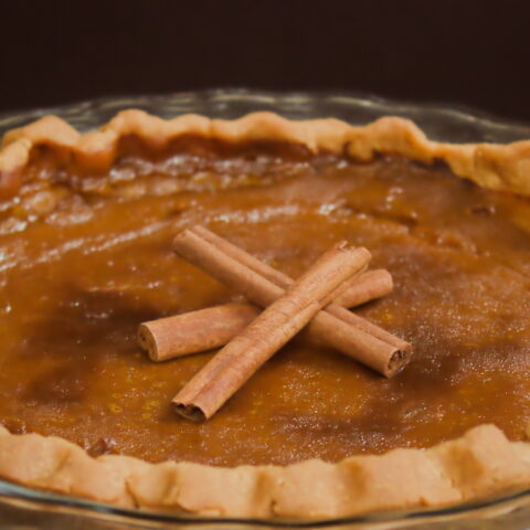 Homemade pumpkin pie in a glass dish topped with cinnamon sticks