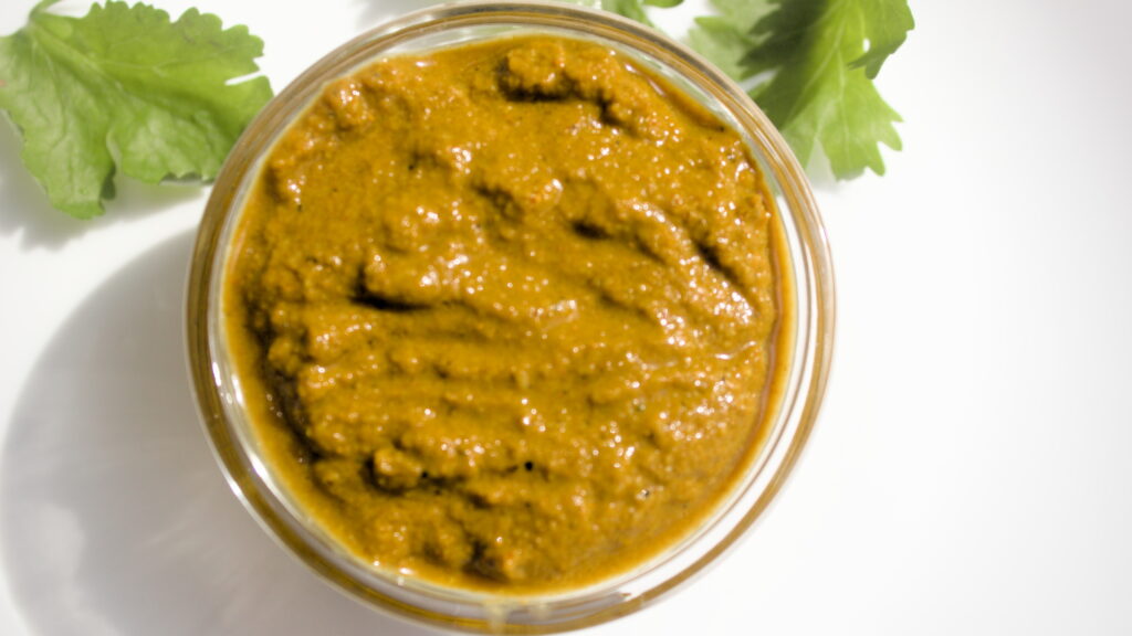 Overhead view of homemade curry paste in a glass bowl, garnished with fresh cilantro leaves on a white background