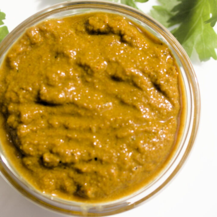 Overhead view of homemade curry paste in a glass bowl, garnished with fresh cilantro leaves on a white background