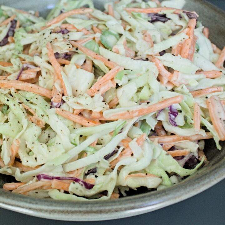 A bowl of fresh homemade coleslaw with shredded green cabbage, carrots, and red cabbage, served in a ceramic bowl on a dark background