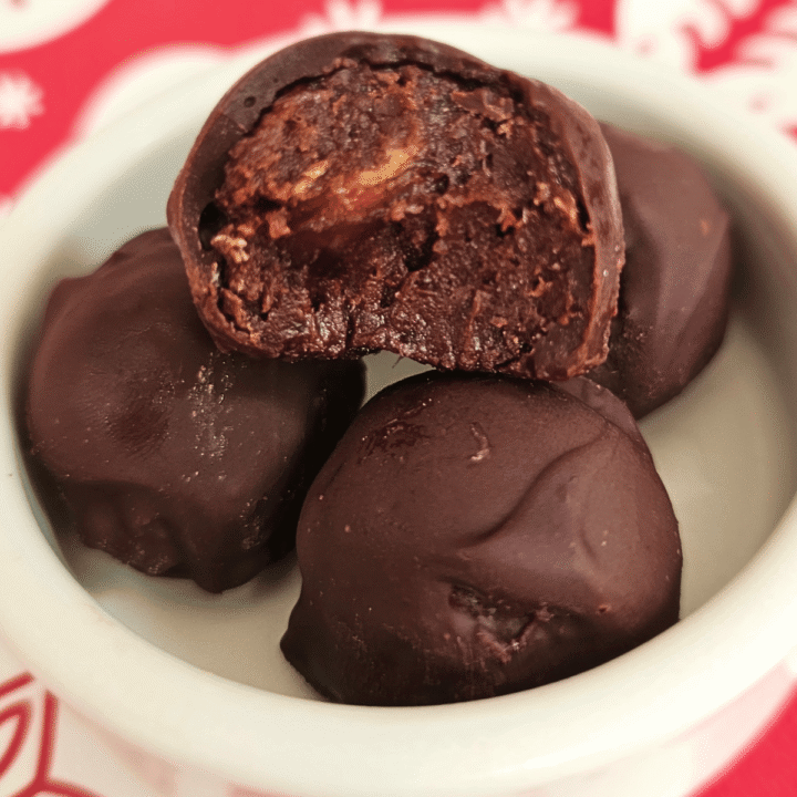 4 date truffles in a white dish, one cut in half showing the soft middle