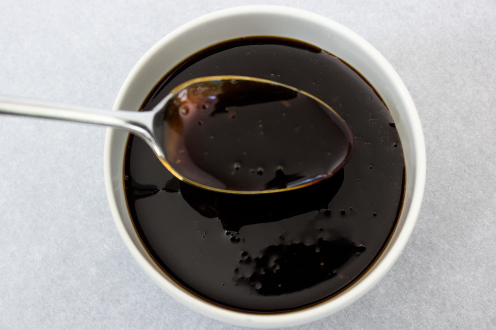 Overhead view of teriyaki sauce in a white bowl with a spoonful of sauce hovering above.