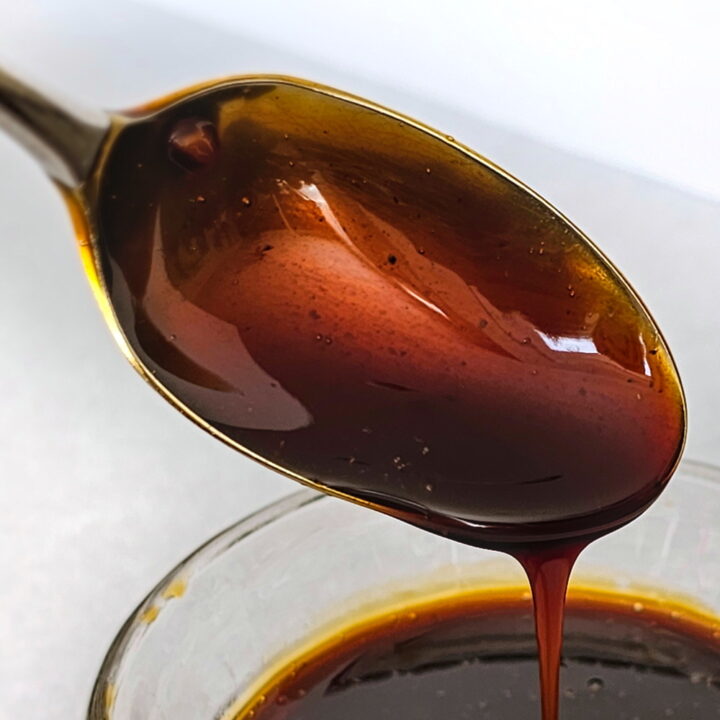 Close up view of spoon coated with teriyaki sauce over a glass bowl
