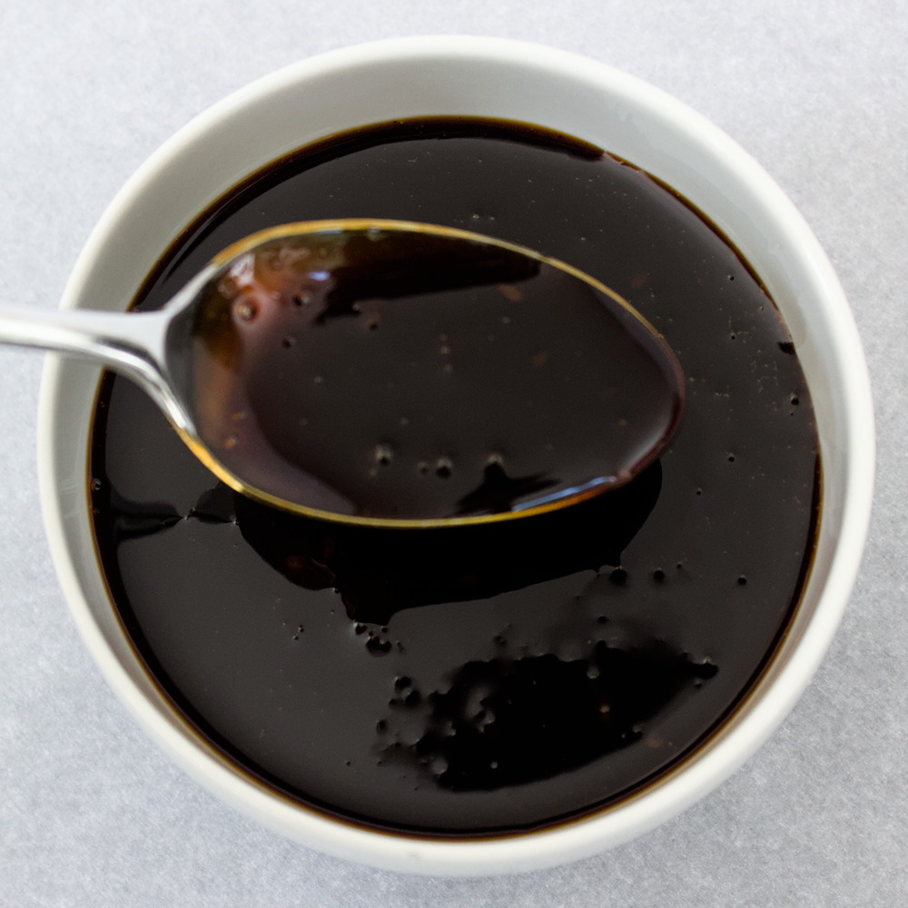 Overhead view of a spoonful of teriyaki sauce over a white bowlful of sauce